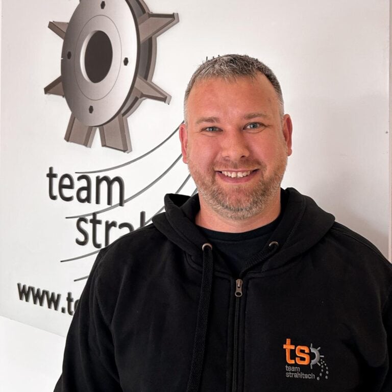 Mann lächelt vor Logo in schwarzem Hoodie, metallisch graues Zahnrad im Hintergrund.